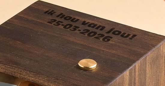 Detail van een donkerhouten flipbook met de gravure "ik hou van jou 25-03-2026" en een messing knop.