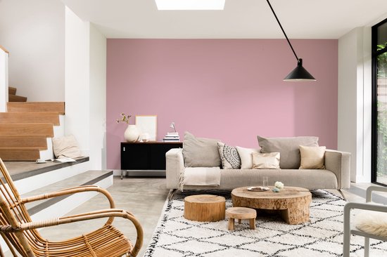 Woonkamer met beige bank, houten salontafels en roze muur.