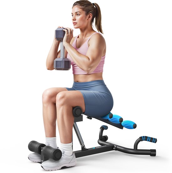 Vrouw met een roze top en blauwe sportbroek zit op een zwart fitnessapparaat met blauwe rollen en houdt een dumbbell vast.
