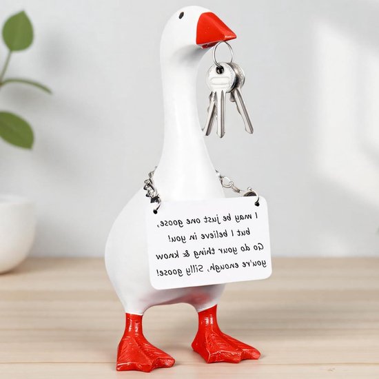 Witte gans met rode snavel en poten, houdt sleutels in de snavel en draagt een bordje met tekst.