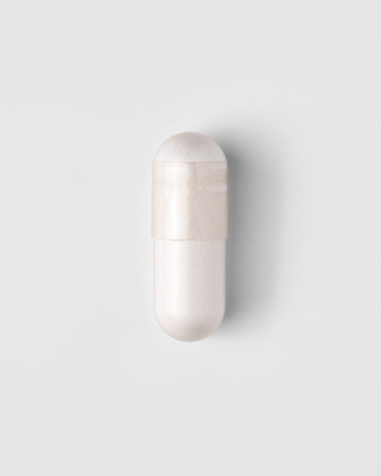 Een enkele witte capsule met een lichte band in het midden, liggend op een witte achtergrond.
