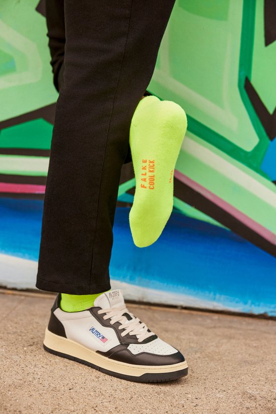 Een felgroene Falke Cool Kick sneakersok uit een zwarte broek. Neon accenten.