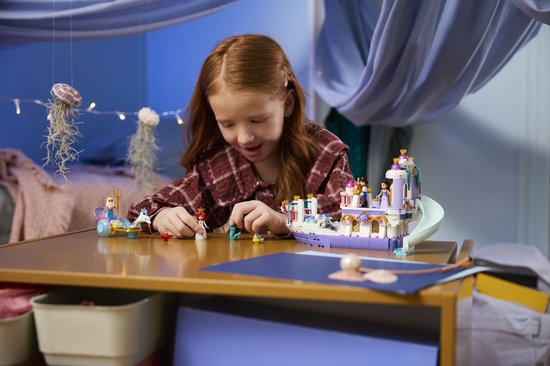 Een jong meisje speelt met de Lego Disney Ariëls Koninklijke Trouwboot set op een houten tafel.