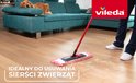 Vileda mop avec manche rouge, enlevant des fibres rouges et blanches d'un plancher en bois, avec un chien sur le canapé.