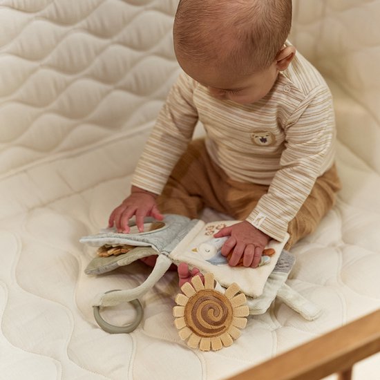 Baby ligt op een witte ondergrond te spelen met het stoffen boekje. Boekje met spiegel, vogel en zonnebloem.