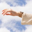 Vrouwenpols met een rosegouden Milanese bandje, tegen een achtergrond van blauwe luchten met wolken.