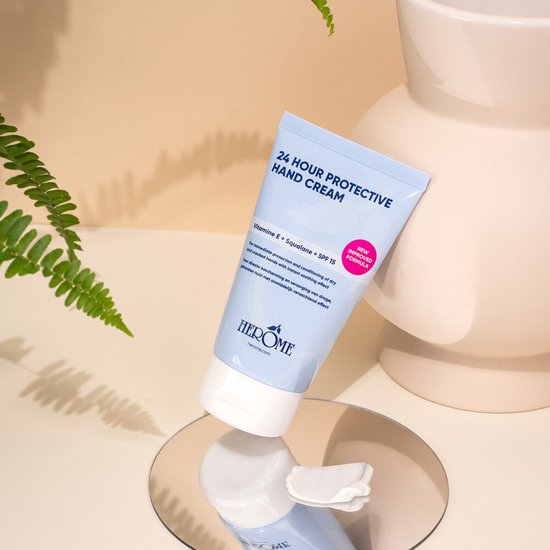 Tube Herome 24 Hour Protective Hand Cream met vitamine E, squalaan en SPF 15, leunend op een spiegel.