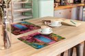 Deux sets de table avec un imprimé d'une maison rose avec une porte bleue, entourée de fleurs colorées, sur une table en bois avec des tasses de café.