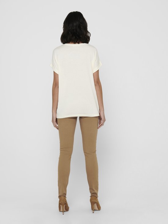 Model in een crèmekleurig T-shirt met opgerolde mouwen en een ronde hals. Draagt een beige skinny broek.