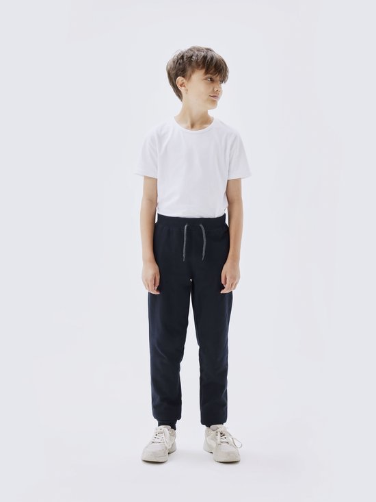 Jongen draagt een navy joggingbroek met grijze veter en witte sneakers.