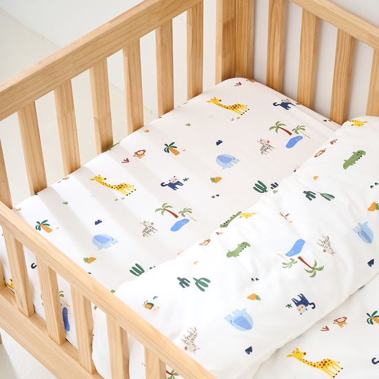 Houten ledikant opgemaakt met beddengoed met safari print van giraffen, olifanten, zebra's, krokodillen en apen.