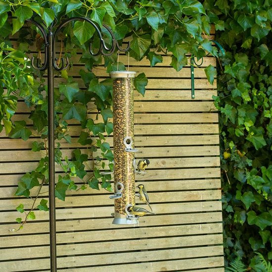 Vogelvoersilo met drie mezen die eten, hangend aan een paal in een tuin.