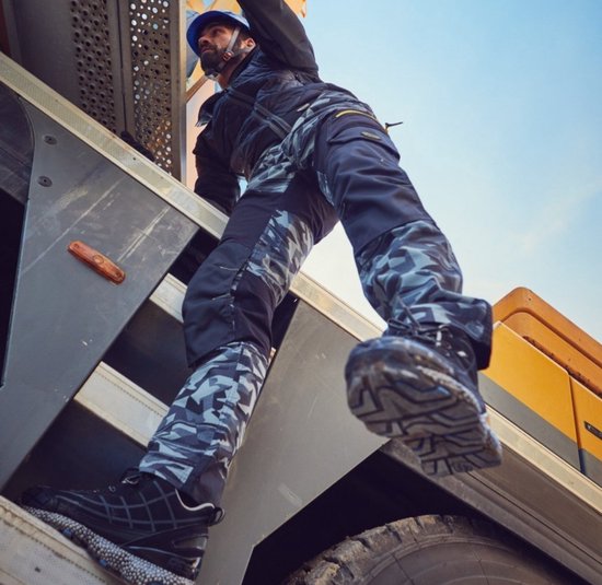 Bouwvakker in camouflage werkbroek klimt op een machine, laag camerastandpunt.
