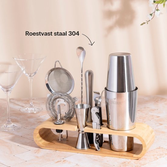 Zilverkleurige cocktailset van roestvrij staal op een bamboe standaard, met martiniglazen op de achtergrond.
