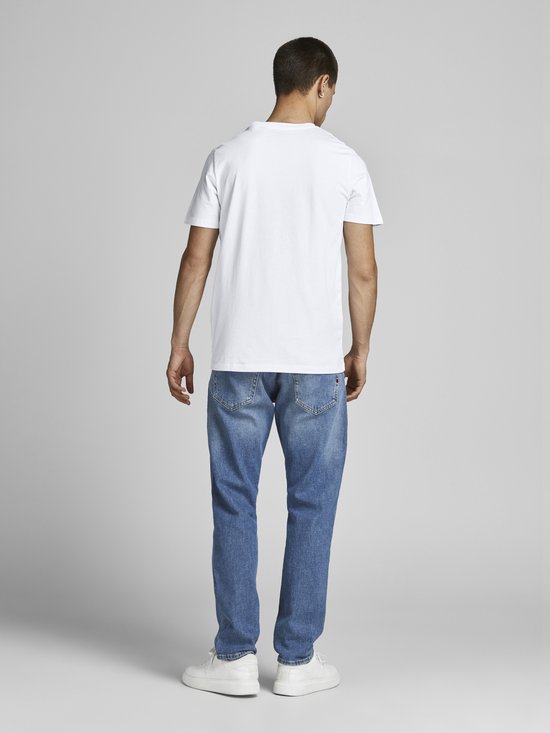 Man in een wit T-shirt en blauwe spijkerbroek, rug zichtbaar, staand.