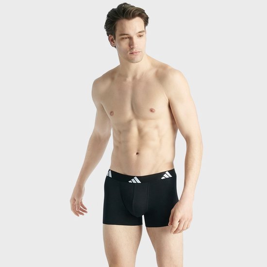 Man in zwarte Adidas boxershort met witte logo's op de band.
