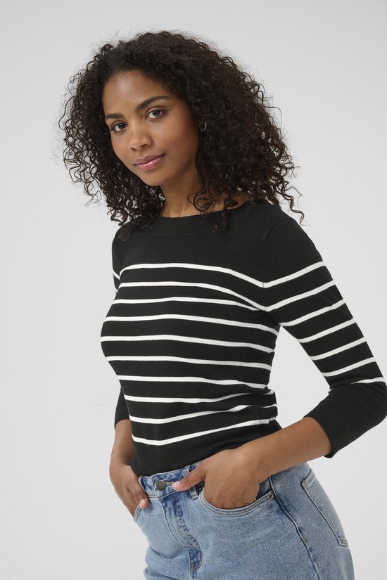 Model met een zwarte trui met horizontale witte strepen en driekwart mouwen, gecombineerd met jeans.