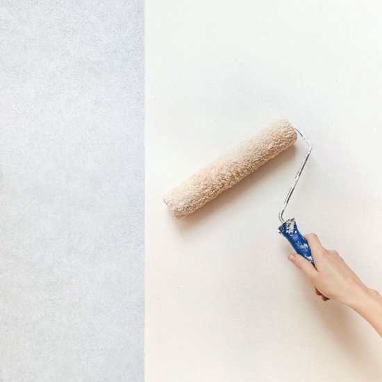 Main avec un rouleau de peinture appliquant de la peinture blanche sur un mur.