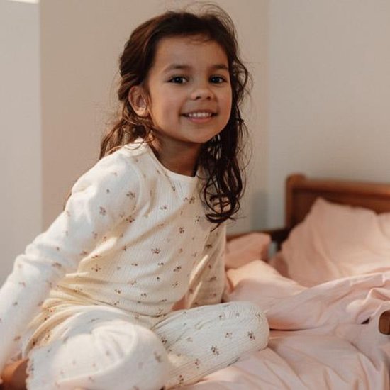 Een meisje zit op een bed in een pyjama met bloemenprint.
