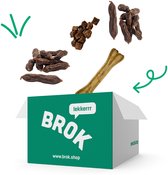Een groene doos van BROK met verschillende hondensnacks eromheen, waaronder worstjes en een bot. "LEKKERRR"
