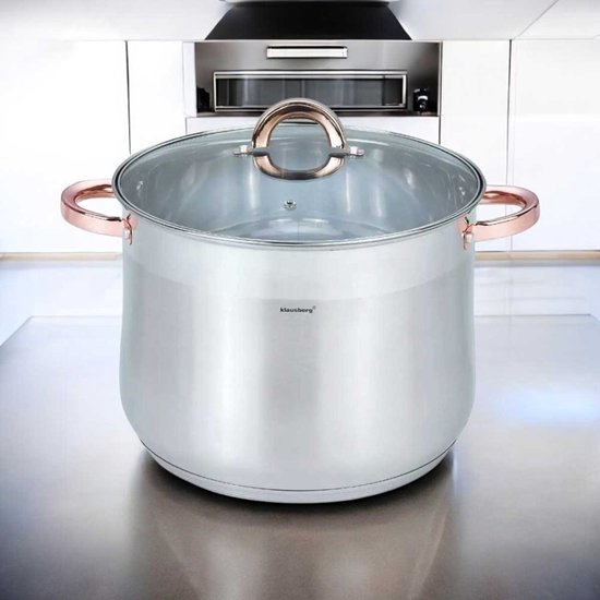 Zilverkleurige soeppan met glazen deksel en koperkleurige handvatten, staand op een aanrecht.