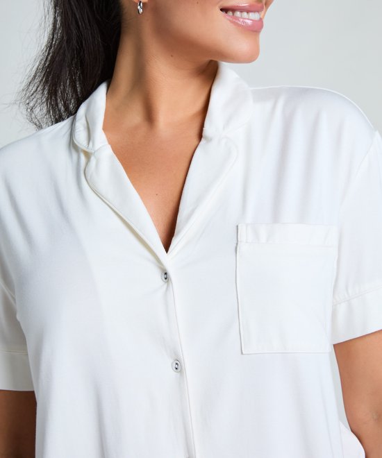 Close-up van een model die een wit pyjamashirt met korte mouwen en kraag draagt, met een glimlach.