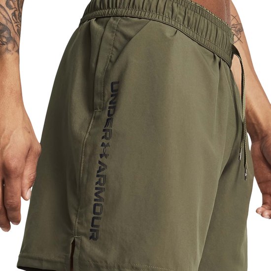 Legergroene shorts met verticale zwarte Under Armour-letters op de linkerpijp