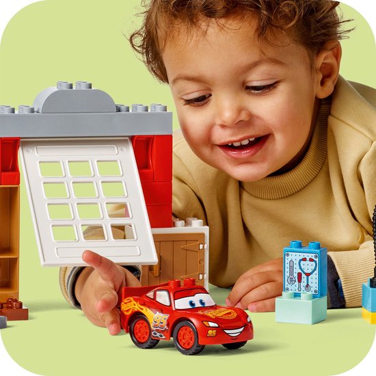 Jongetje speelt met de rode LEGO Duplo Lightning McQueen en de doktersgarage. Hij houdt een stukje van de garage vast.