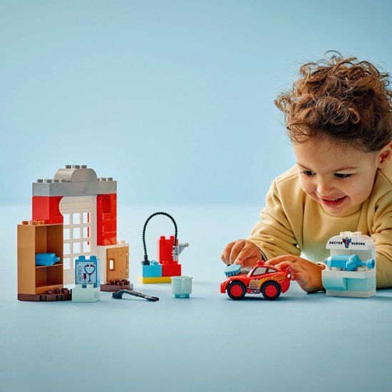 Jongetje met LEGO Duplo Cars set: rode Lightning McQueen, doktersgarage, gereedschap, op een blauwe ondergrond.