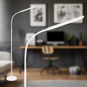 Witte staande lamp in een woonkamer, voor een bureau met computer en schilderijen aan de muur.