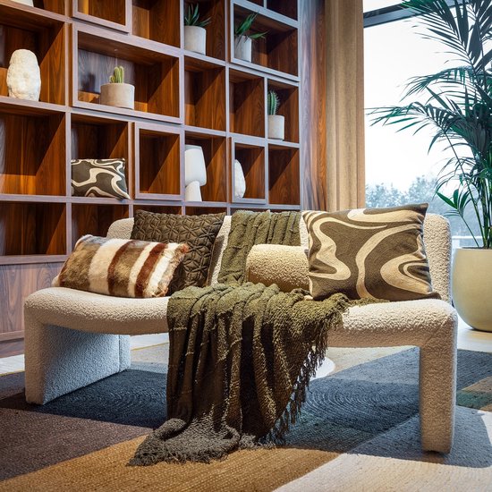 Off-white bank met meerdere kussens en plaids in verschillende texturen en patronen in olijfgroene en bruine tinten.