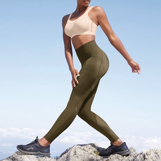 Model in een beige sportbeha en olijfgroene legging, wandelend op rotsen.
