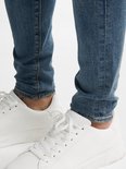 Detail van een man met blauwe skinny jeans en witte sneakers.