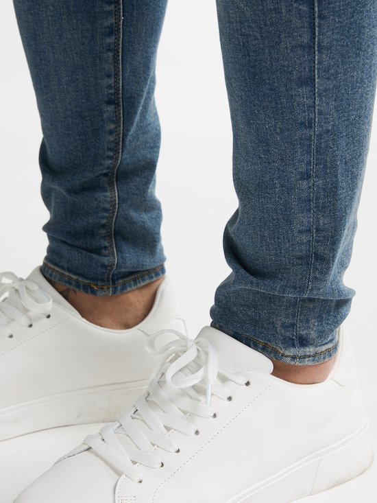Detail van een man met blauwe skinny jeans en witte sneakers.