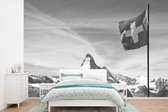 Behang - Fotobehang Zwitserse Vlag bij Matterhorn in Zwitserland - zwart wit - Breedte 330 cm x hoogte 220 cm