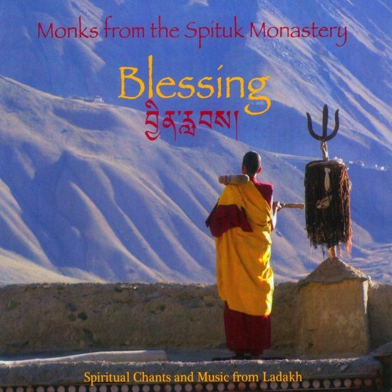 Een monnik in geel en bordeauxrood gewaad draagt een staf, met een rituele stok ernaast. Boven aan de tekst: Monks from the Spituk Monastery, Blessing (Tibetaanse karakters). Onderaan: Spiritual Chants and Music from Ladakh.