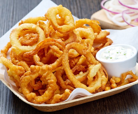 Een mandje met goudbruine, krokant gebakken uienringen, geserveerd met dipsaus.