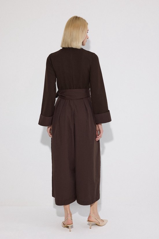 Donkerbruine jumpsuit met strikceintuur en wijde broekspijpen, gezien vanaf de achterkant. Model draagt een coltrui met lange mouwen.