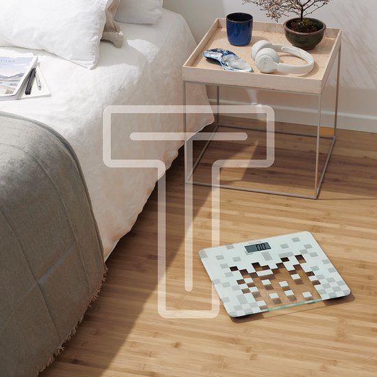 Witte digitale weegschaal met pixelpatroon op een houten vloer naast een bed.