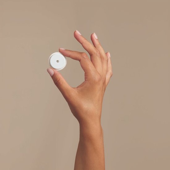 Hand van een vrouw die een kleine, ronde, witte glucosesensor vasthoudt.