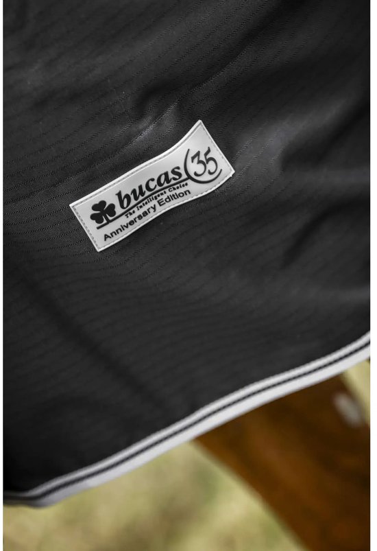 Detail van het Bucas Anniversary Edition label op een zwarte, geweven deken.