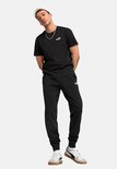 Man draagt een zwarte PUMA t-shirt en zwarte trainingsbroek, met een witte pet.
