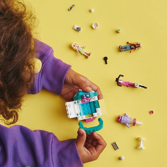 Kinderhanden bouwen aan LEGO Friends bubbelthee kar, met poppetjes en accessoires op gele achtergrond.