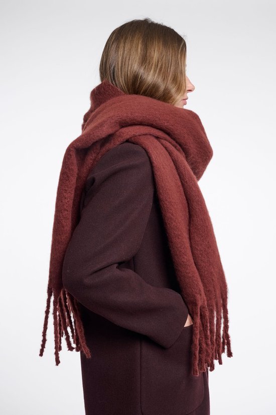 Zijaanzicht van een vrouw met een oversized, donkerrode sjaal met franjes om haar nek.