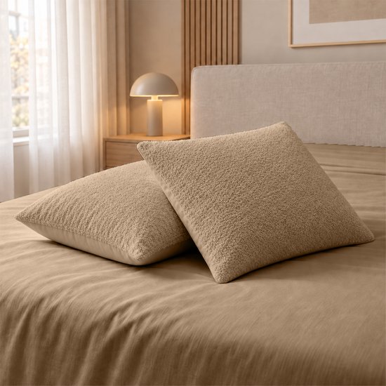 Twee taupe teddy kussens op een bed met een taupe laken.