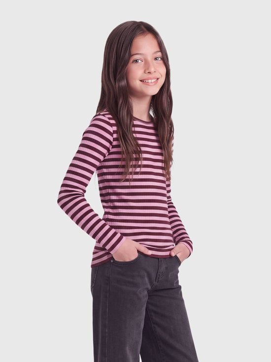Model glimlacht met handen in de zakken, draagt een geribbelde top en zwarte jeans.
