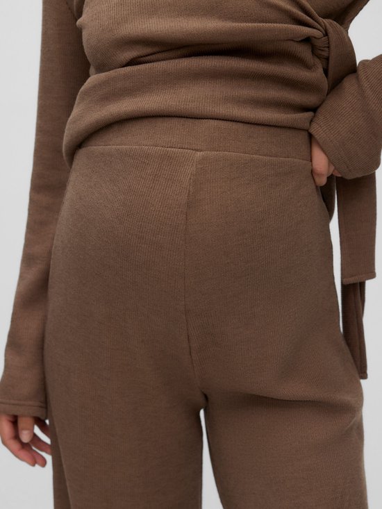 Close-up van de bruine, fijngebreide zwangerschapsbroek met hoge taille en een bijpassende wikkel-top.