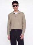 Close-up van model in beige gebreide polo met zwarte broek en riem.