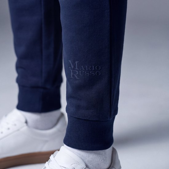 Detailopname van de marineblauwe joggingbroek met Mario Russo-tekst in reliëf bij de enkel.