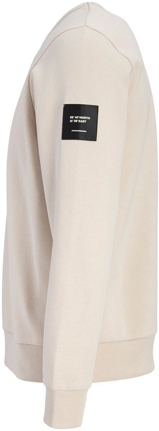Zijaanzicht van een crème kleurige sweater met een zwart label op de mouw met witte coördinaten en tekst.